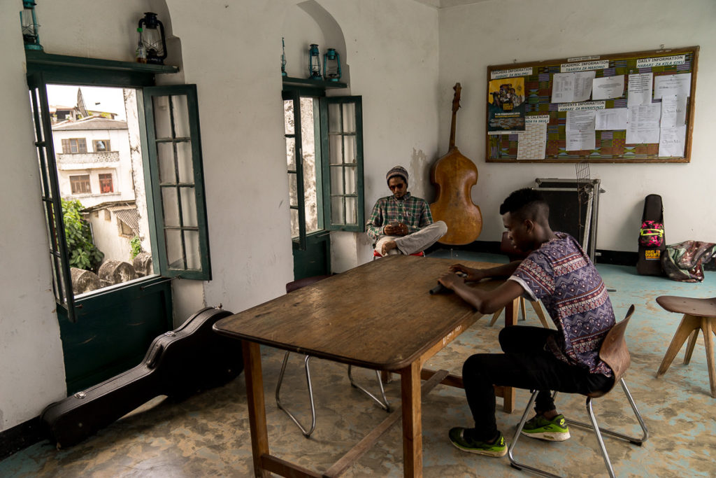 Tanzania, Zanzibar, Stone Town. An enterprising hat maker with an  eye-catching display on the wall of the old Omani Fort bargains with a  passing tourist. - SuperStock